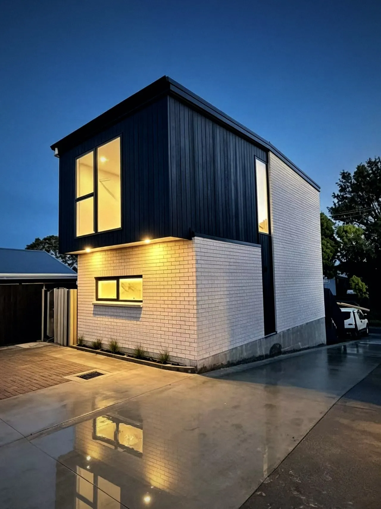 Black vertical cladding over white brick at dusk
